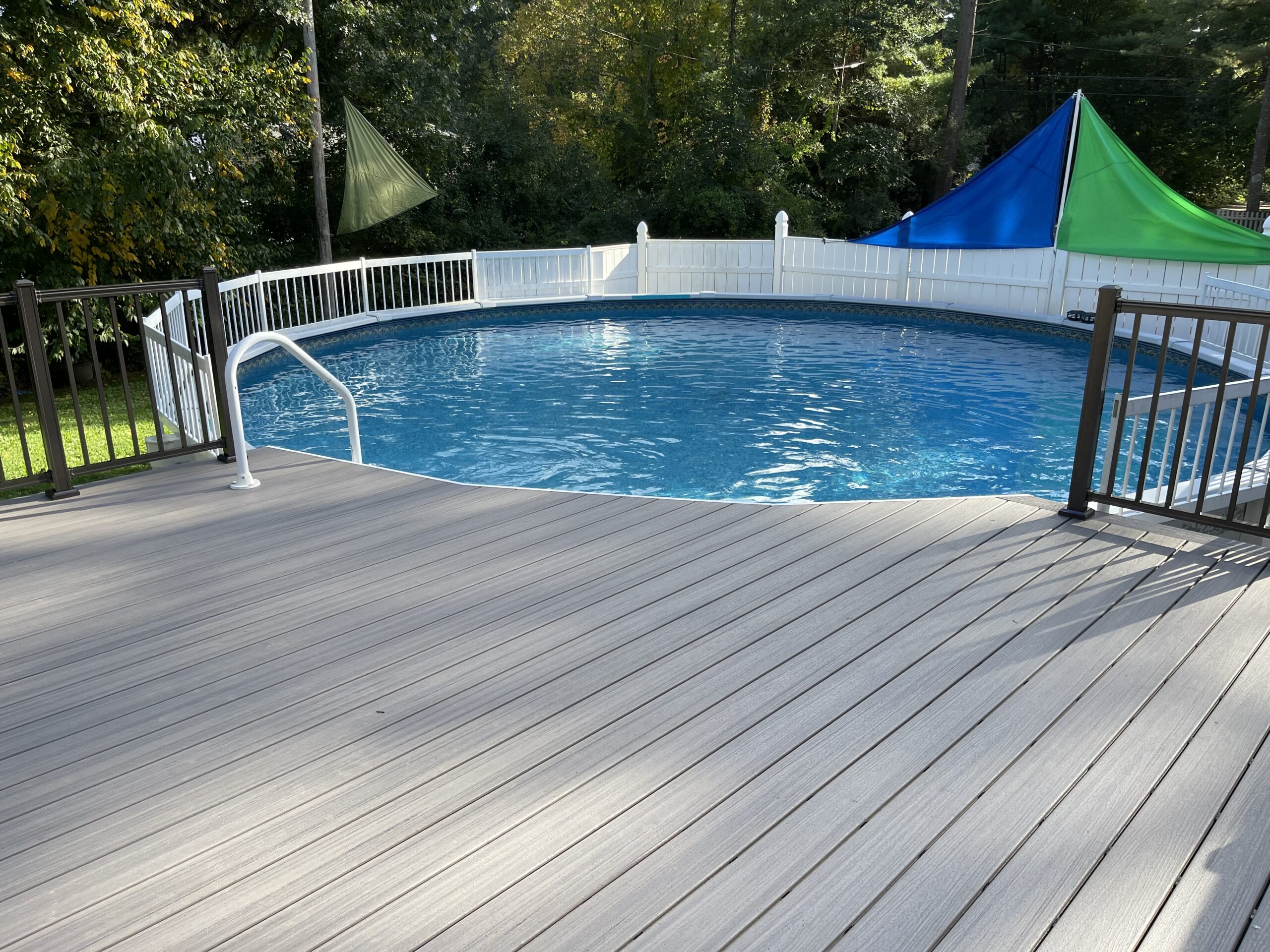 Modern composite deck material with sleek aluminum railings, adjacent to a glistening outdoor pool, complete with chic loungers and lush greenery, epitomizing luxury outdoor living.